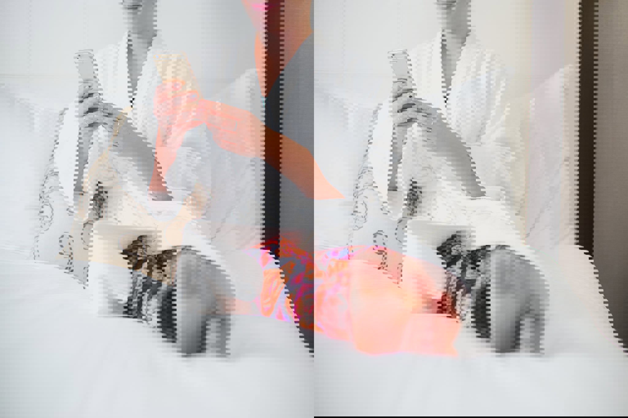 a woman in a bathrobe sits on a bed looking at her phone