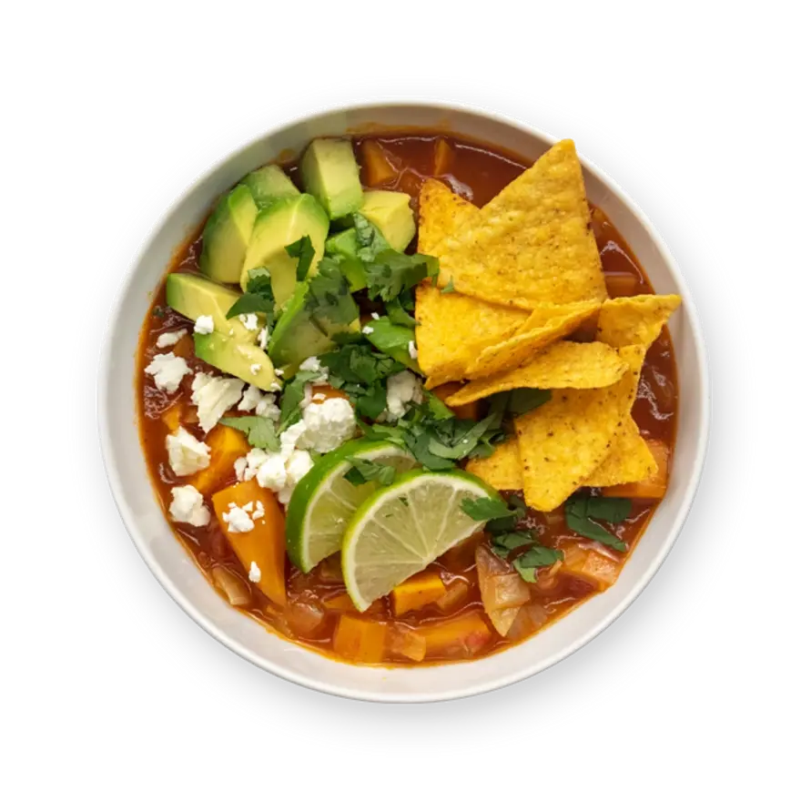 a bowl of soup with tortilla chips , avocado , cheese and lime wedges