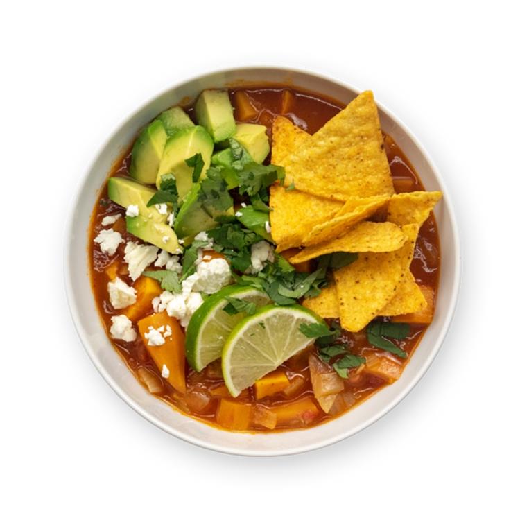 a bowl of soup with tortilla chips , avocado , cheese and lime wedges
