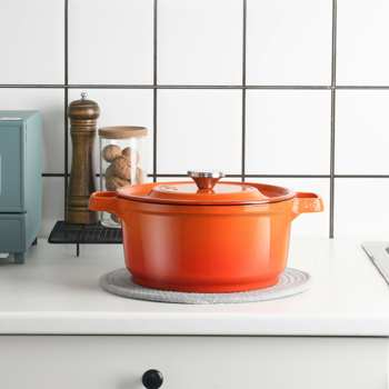 an orange Dutch oven sits on a counter next to a jar of walnuts