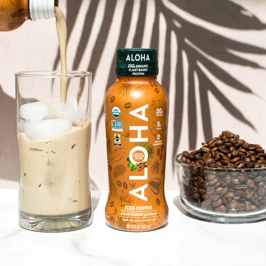 a bottle of aloha iced coffee is being poured into a glass next to a bowl of coffee beans