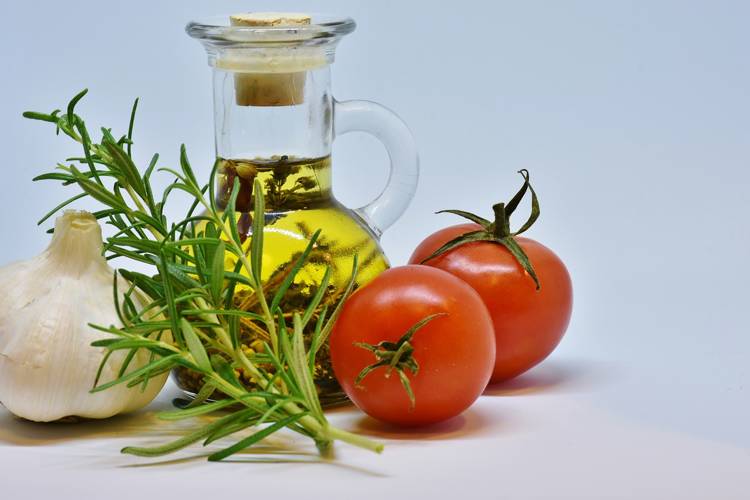 a bottle of olive oil sits next to tomatoes and garlic
