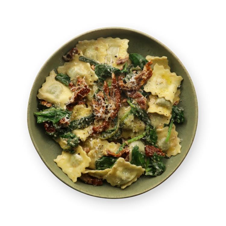 a bowl of ravioli with spinach and sun dried tomatoes on a white background