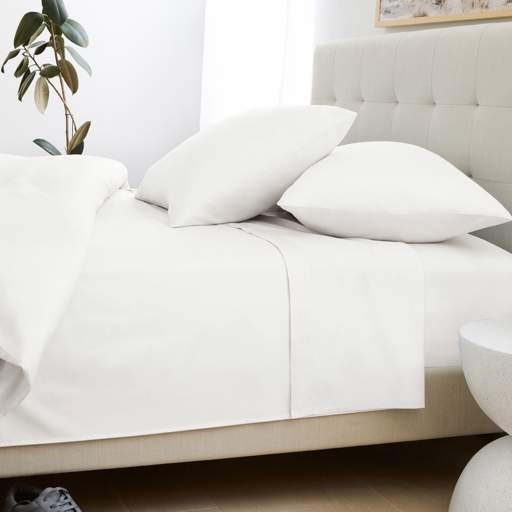 a bed with white sheets and pillows in a bedroom