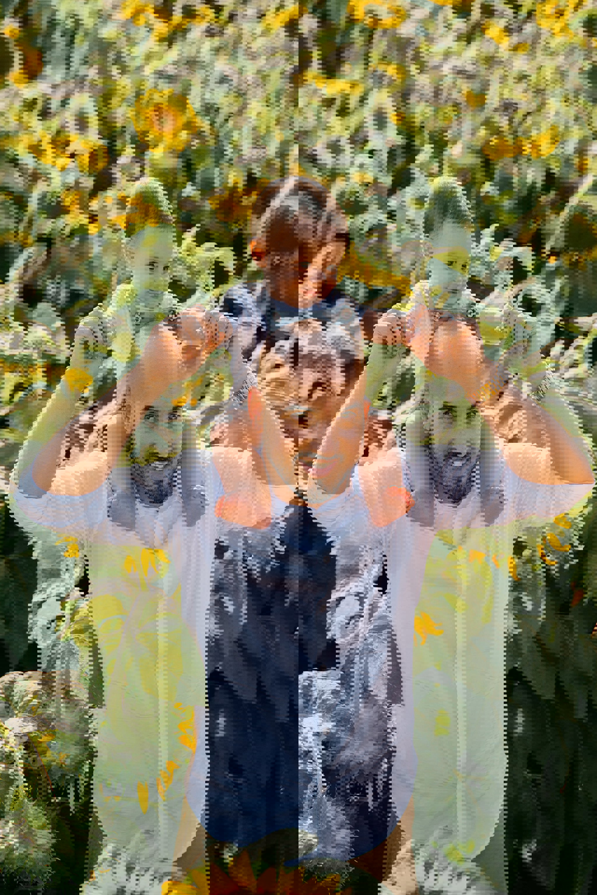a man is carrying a baby on his shoulders in a field of sunflowers