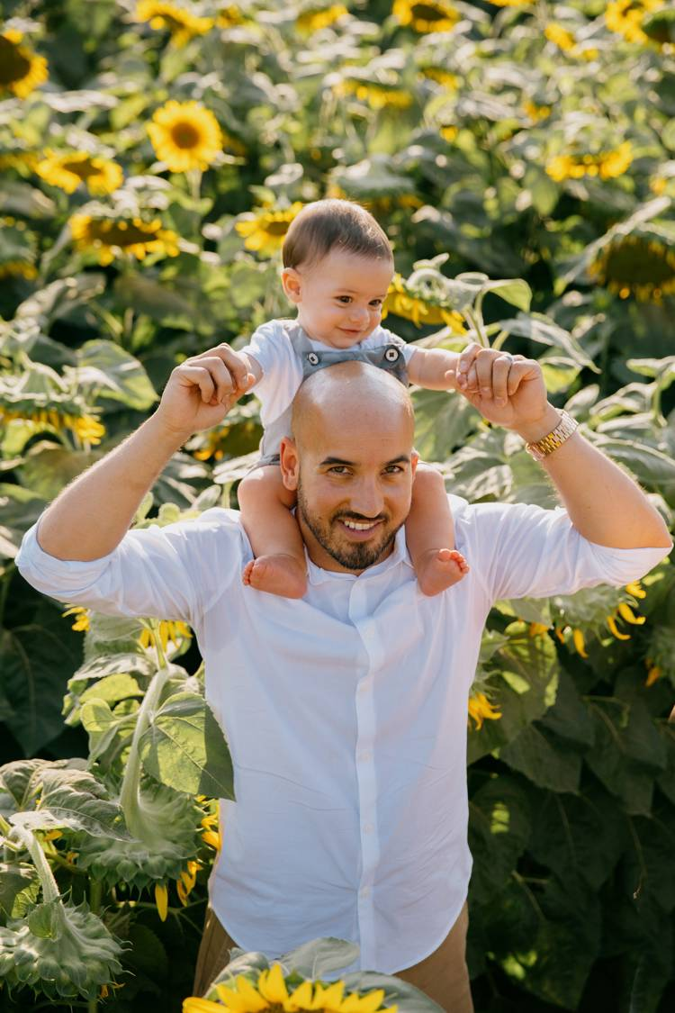 a man is carrying a baby on his shoulders in a field of sunflowers