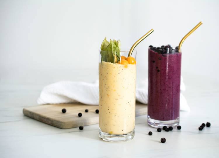 two smoothies in tall glasses with gold straws on a table