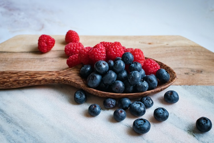 a wooden spoon filled with blueberries and raspberries