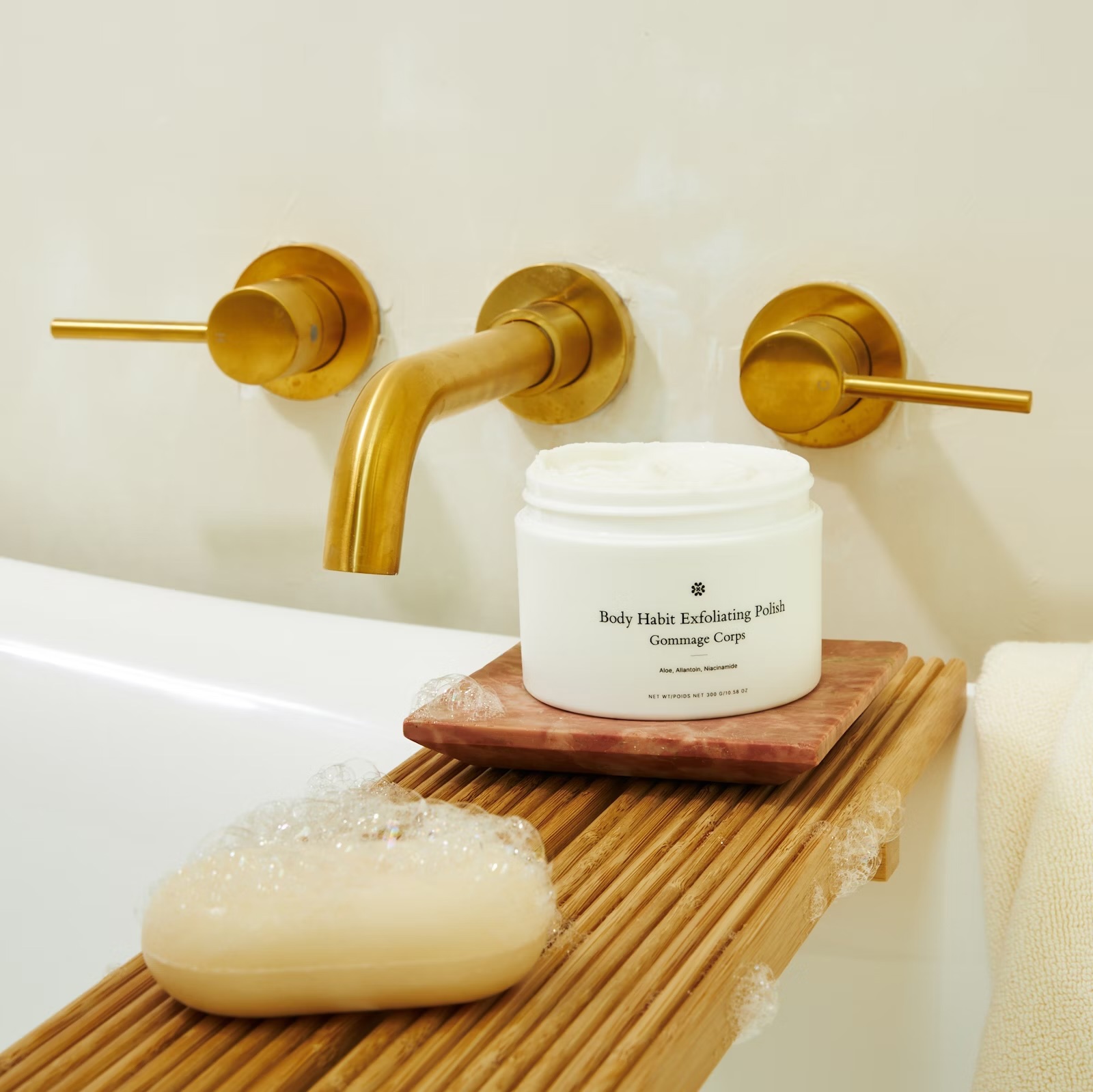 a jar of body habit exfoliating polish sits on a wooden tray next to a bar of soap