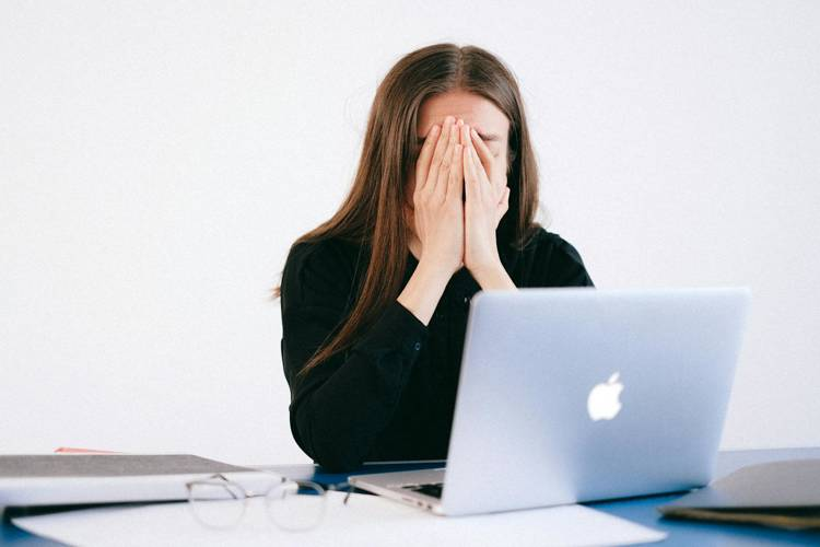 a woman is covering her face while sitting in front of an apple laptop