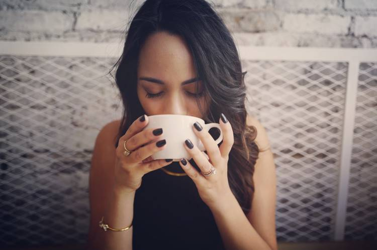 a woman with black nails is drinking from a white cup