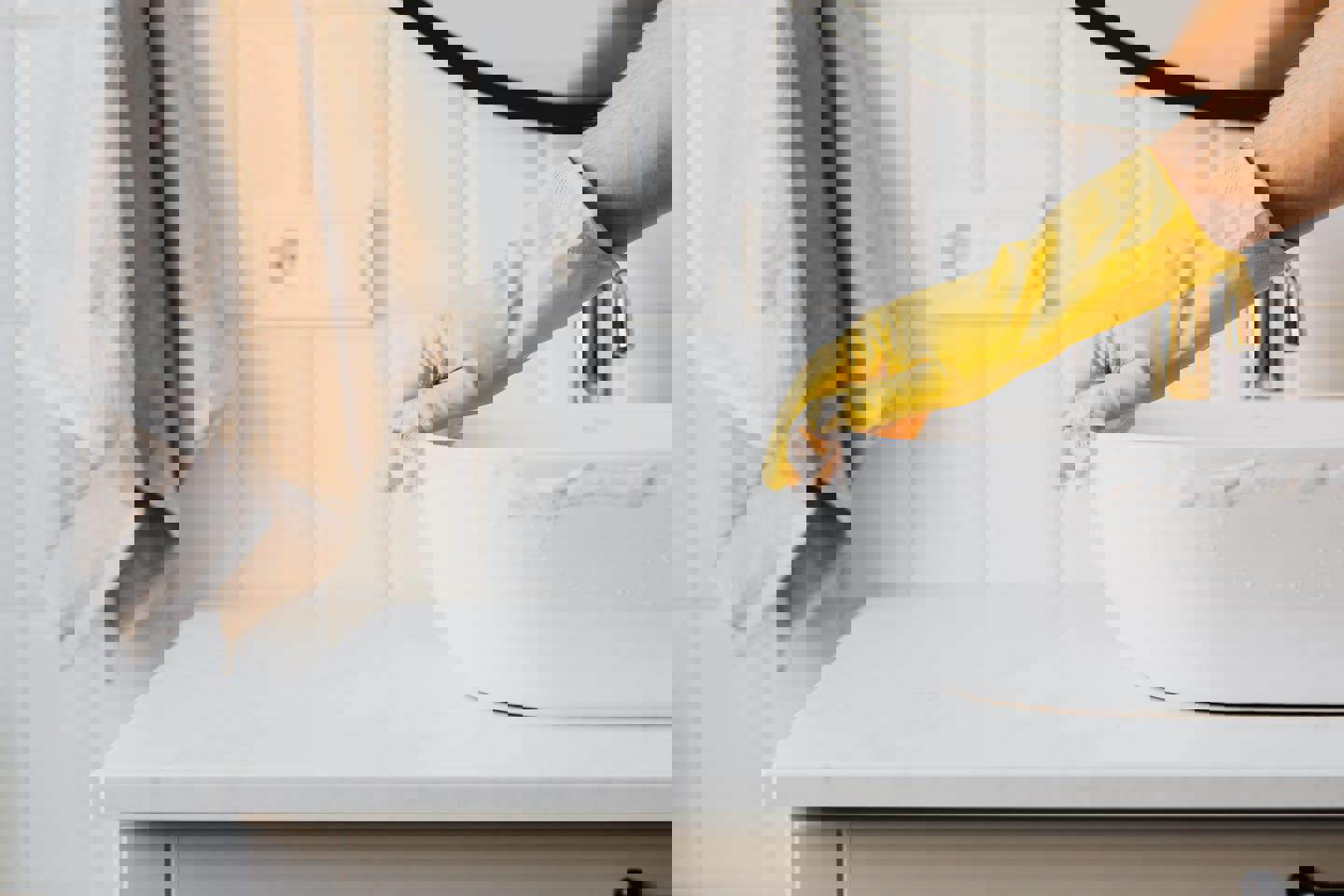a person wearing yellow gloves is cleaning a bathroom sink