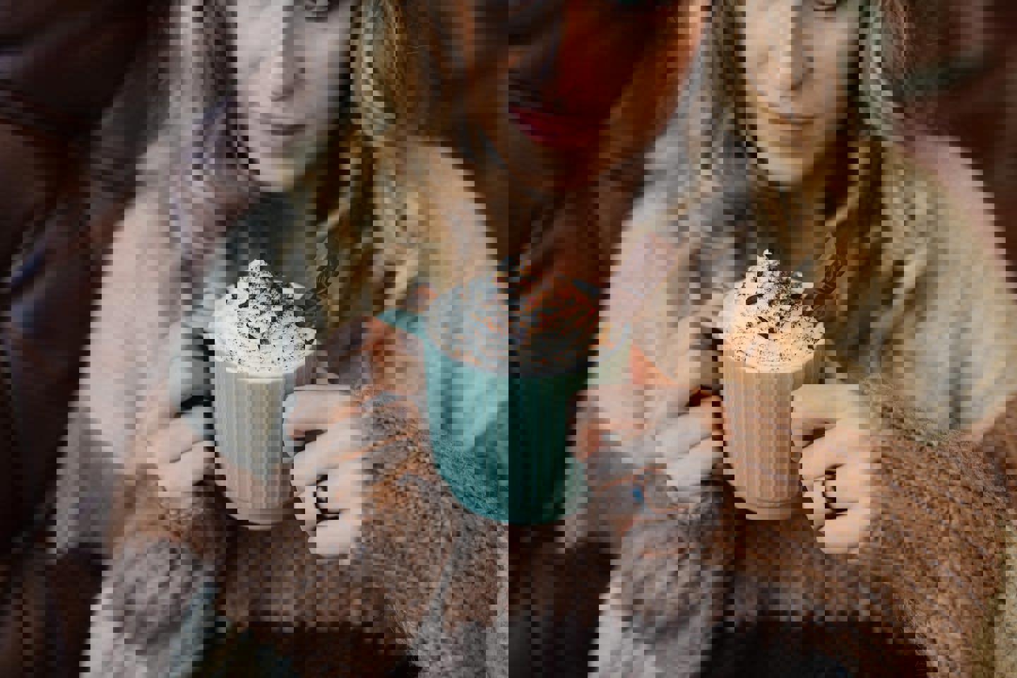 a woman is holding a cup of hot chocolate with whipped cream and chocolate shavings