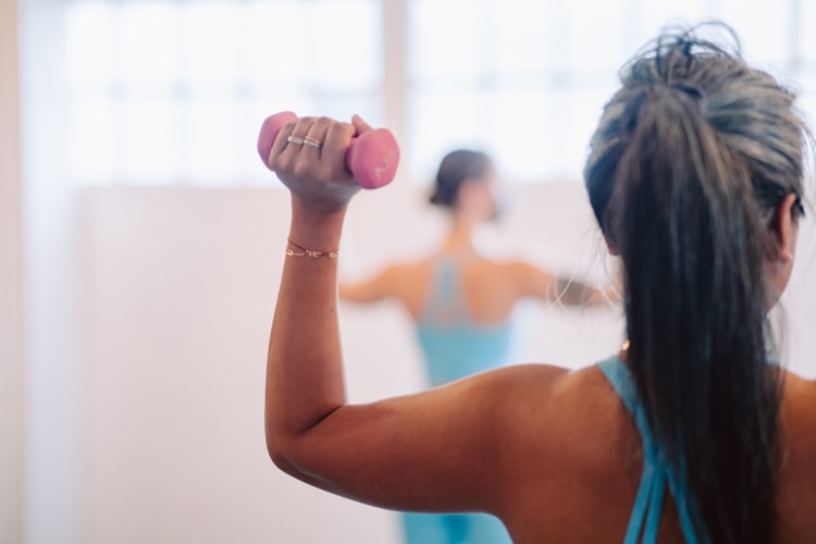 a woman in a blue tank top is lifting a pink dumbbell