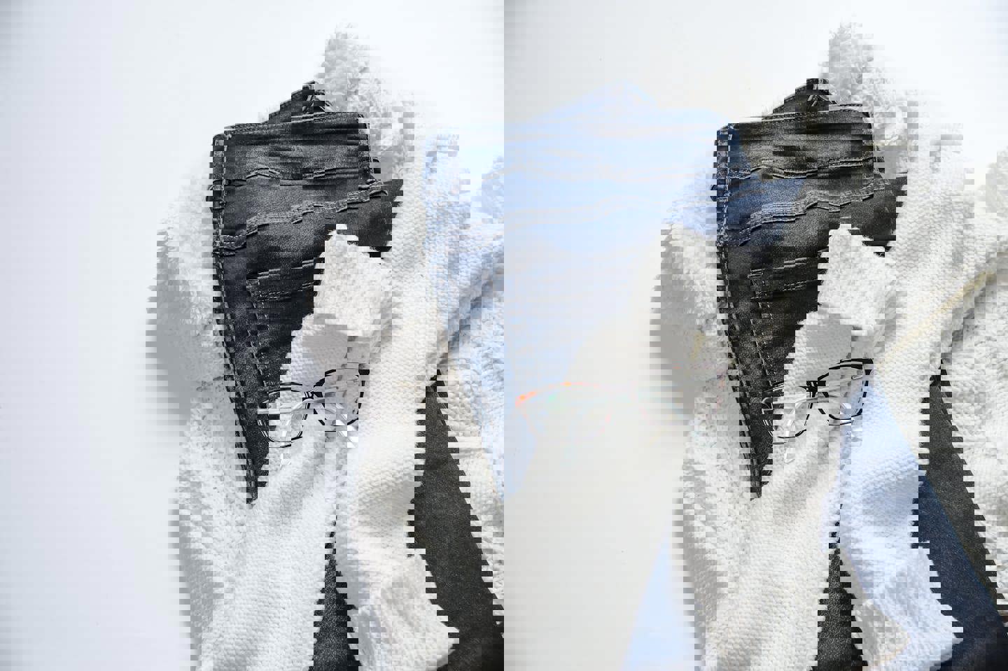 a white sweater , blue jeans , a white sweater and glasses on a white background