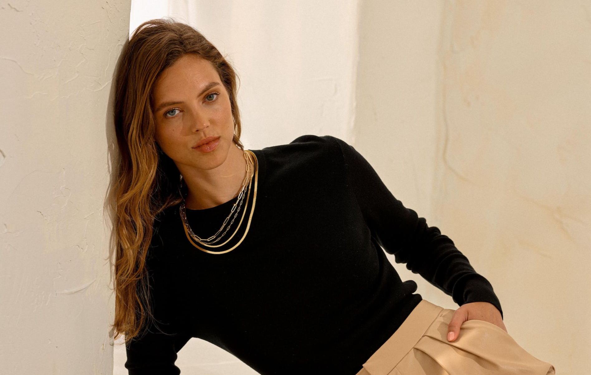 a woman wearing a black sweater and tan shorts is leaning against a wall