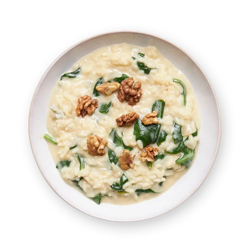 a bowl of risotto with spinach and walnuts on a black background
