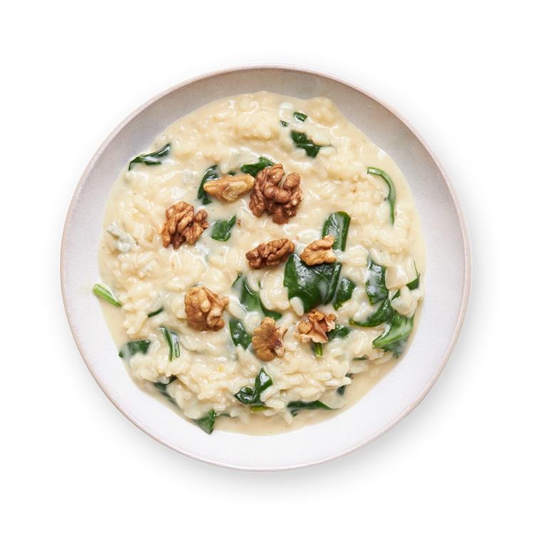 a bowl of risotto with spinach and walnuts on a black background