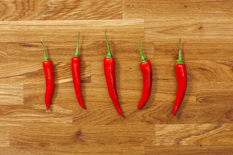five red peppers are lined up on a wooden surface