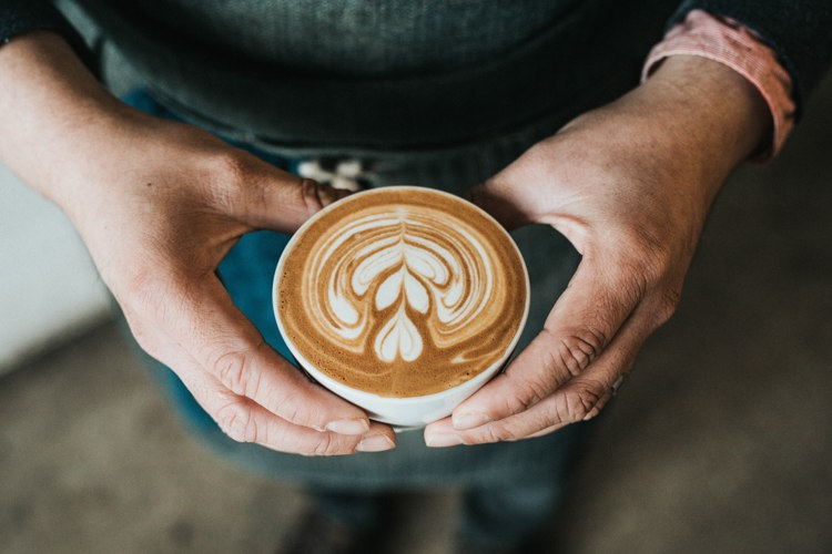 a person is holding a cup of cappuccino with a leaf design on the foam