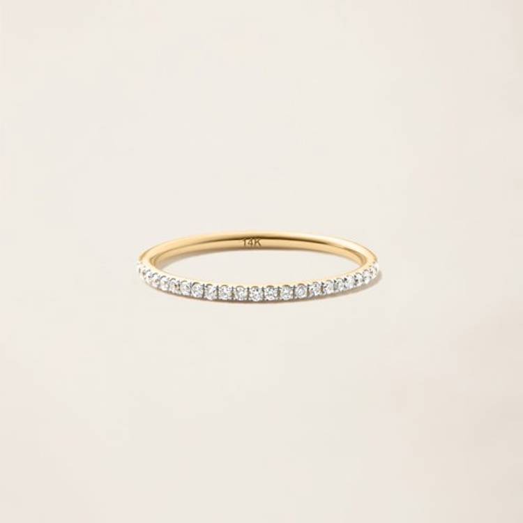 a yellow gold ring with a row of diamonds on a white surface