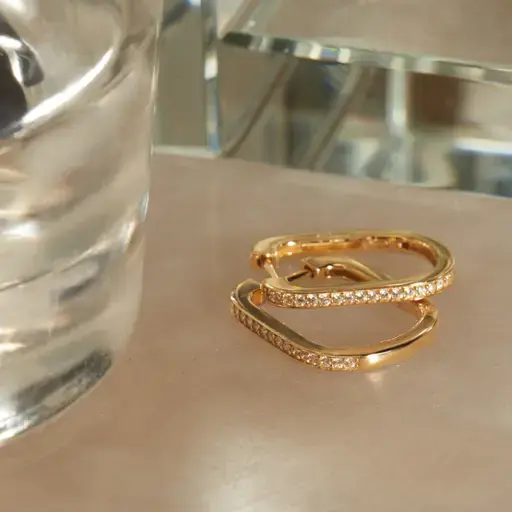 a pair of gold hoop earrings are sitting on a table next to a glass