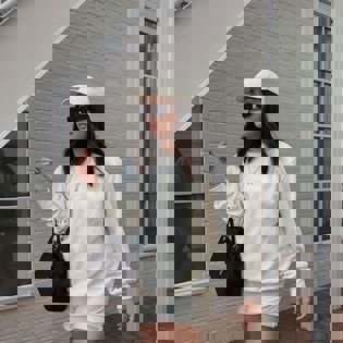 a woman wearing a white sweatshirt and shorts is standing in front of a white brick building