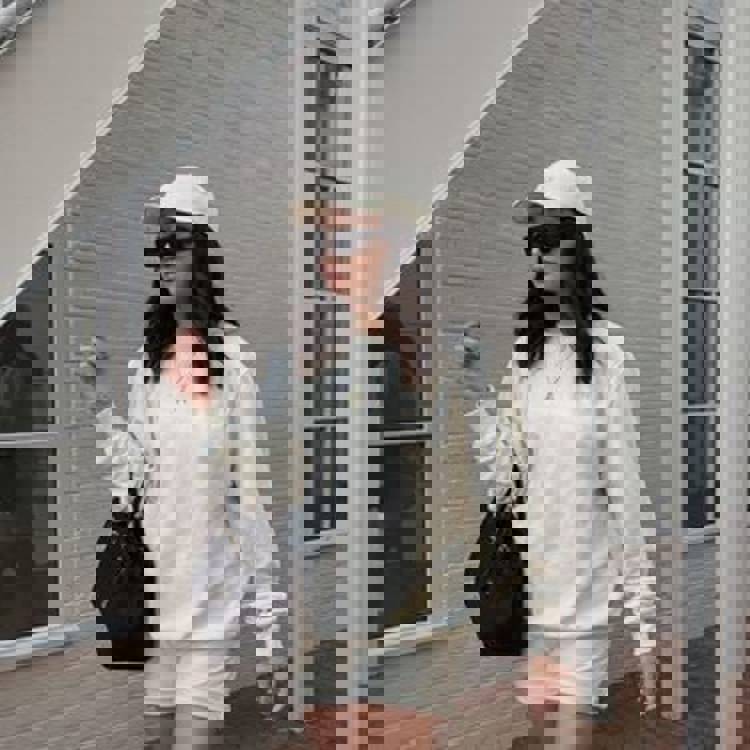 a woman wearing a white sweatshirt and shorts is standing in front of a white brick building