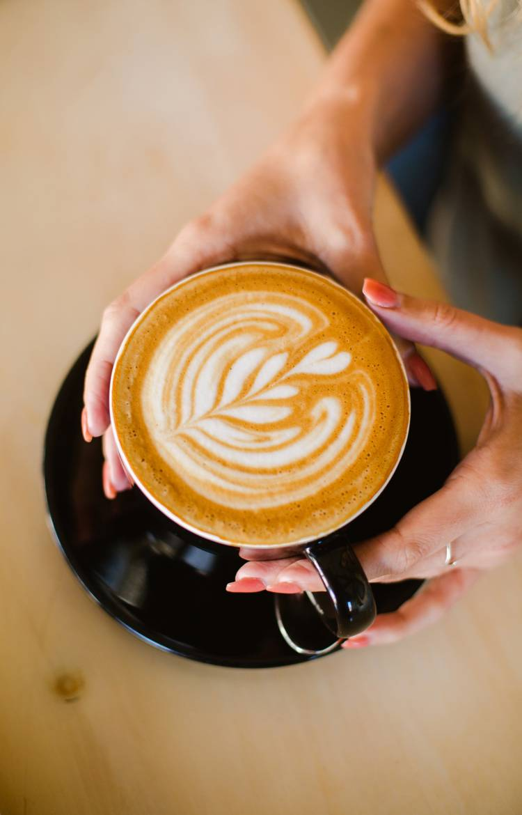a woman holds a flat white with a fern leaf design on the foam