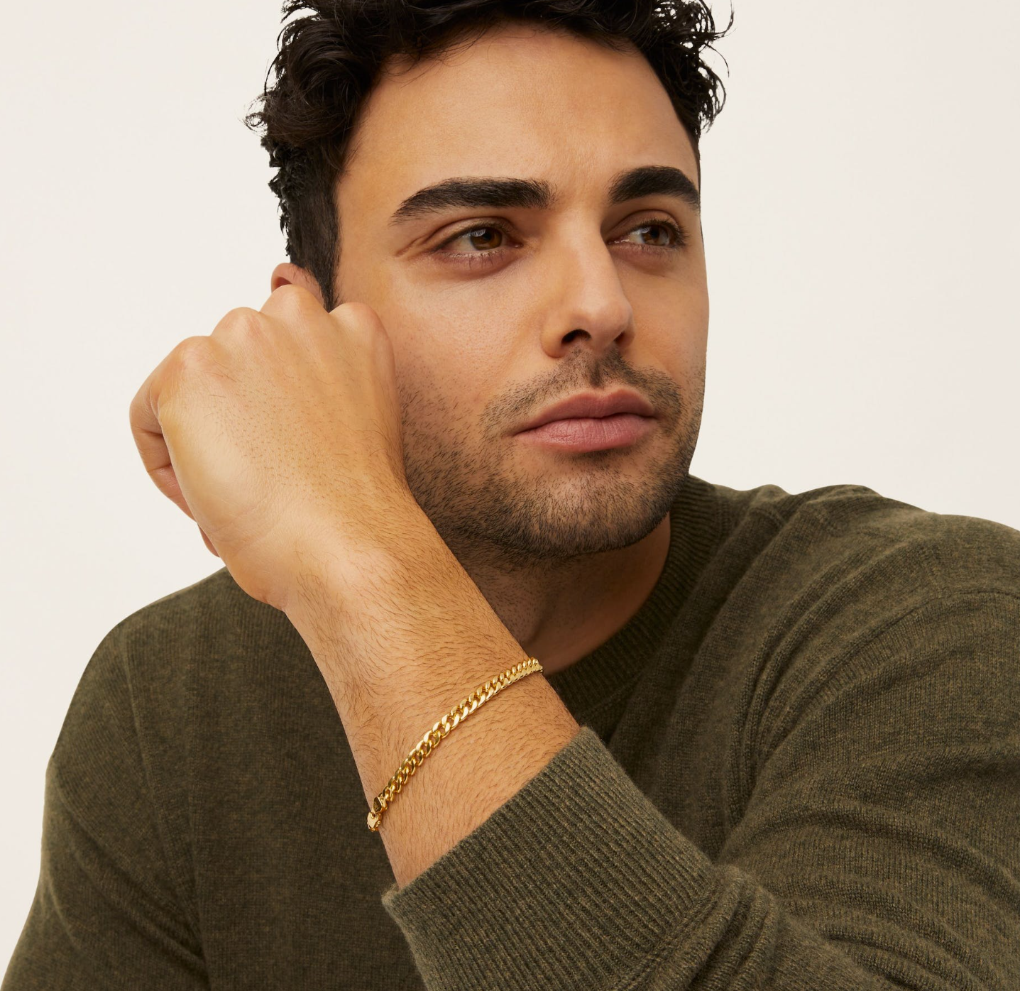 a man wearing a green sweater and a gold bracelet on his wrist