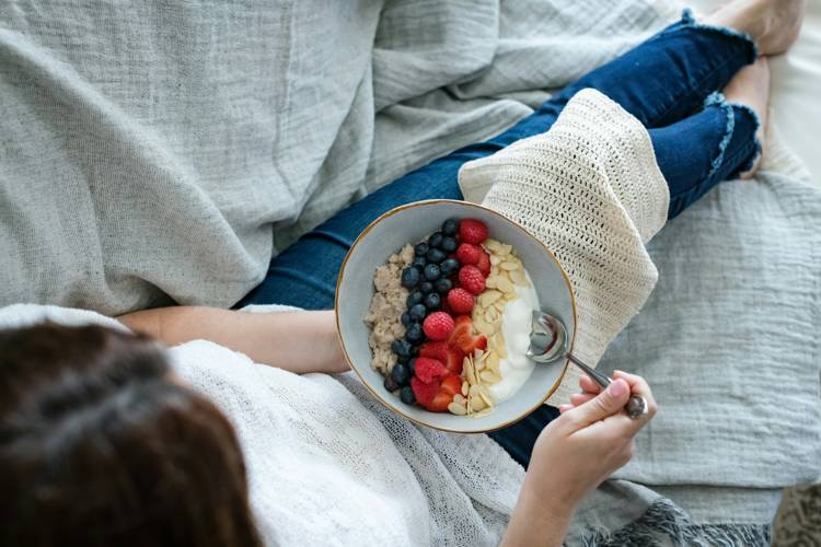 a woman is eating a bowl of oatmeal with berries and yogurt
