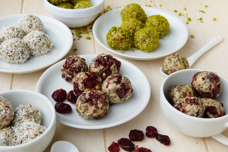 a table topped with plates and bowls of food including cranberry pistachio and coconut balls