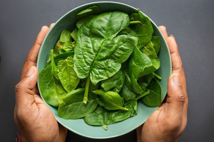 a person is holding a bowl of spinach in their hands