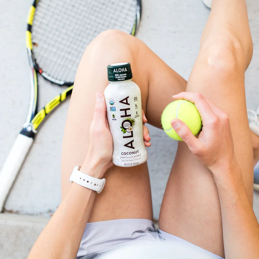 a woman is holding a tennis ball and a bottle of aloha coconut water