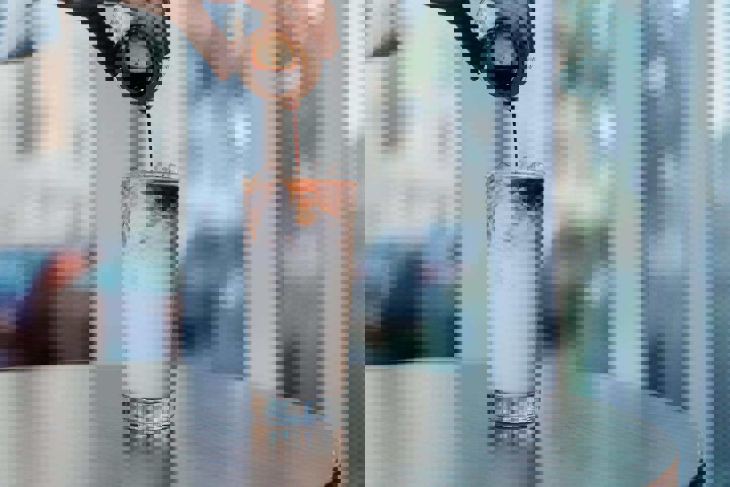 a person is pouring coffee into a glass of iced coffee