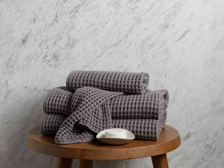 a stack of towels sits on a wooden stool next to a soap dish